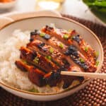 Wooden chopsticks lifting chicken bulgogi from a white bowl or rice.