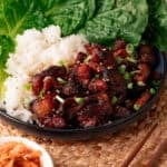 Charred pork bulgogi on a blue plate topped with green onions with white & lettuce.