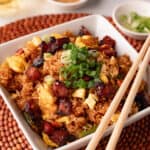 Pork fried rice in a white square bowl with wooden chopsticks.