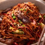 Beef lo mein topped with green onions in a white serving plate.