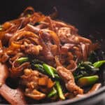 Chicken pad see ew cooking in a wok with a wooden spoon.