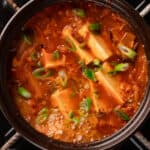 Kimchi soup boiling in a clay pot topped with green onions.