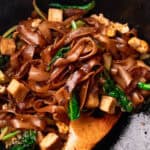 Tofu pad see ew cooking in a wok with a wooden spoon.