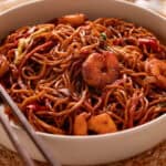 Shrimp lo mein in a white serving plate on a wood dinner table.
