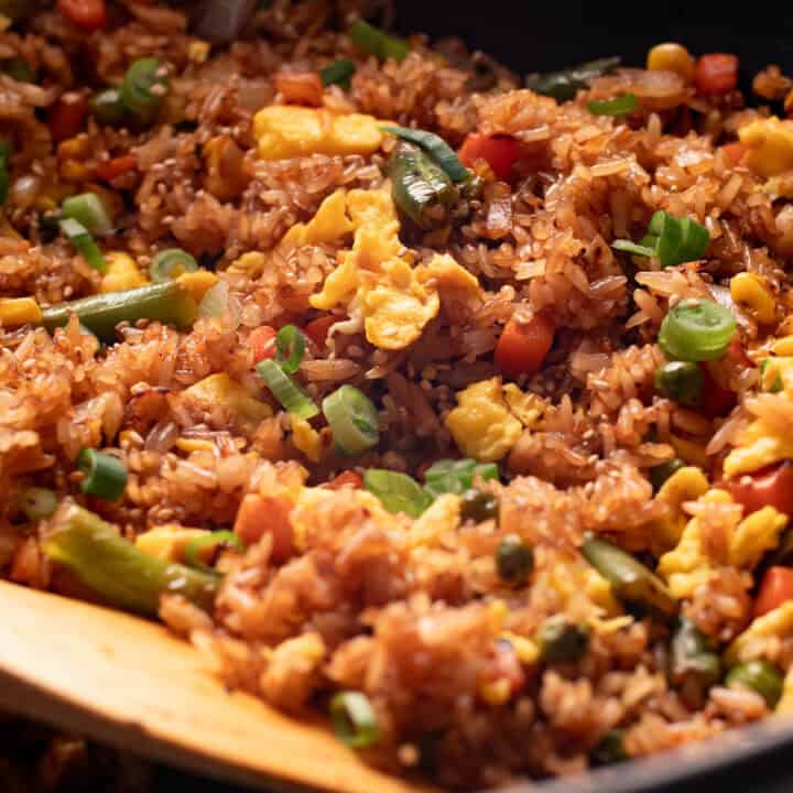 Veggie fried rice with eggs in a wok with a wooden spatula.