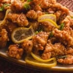 Plate of Chinese lemon chicken with lemon slices and green onions.