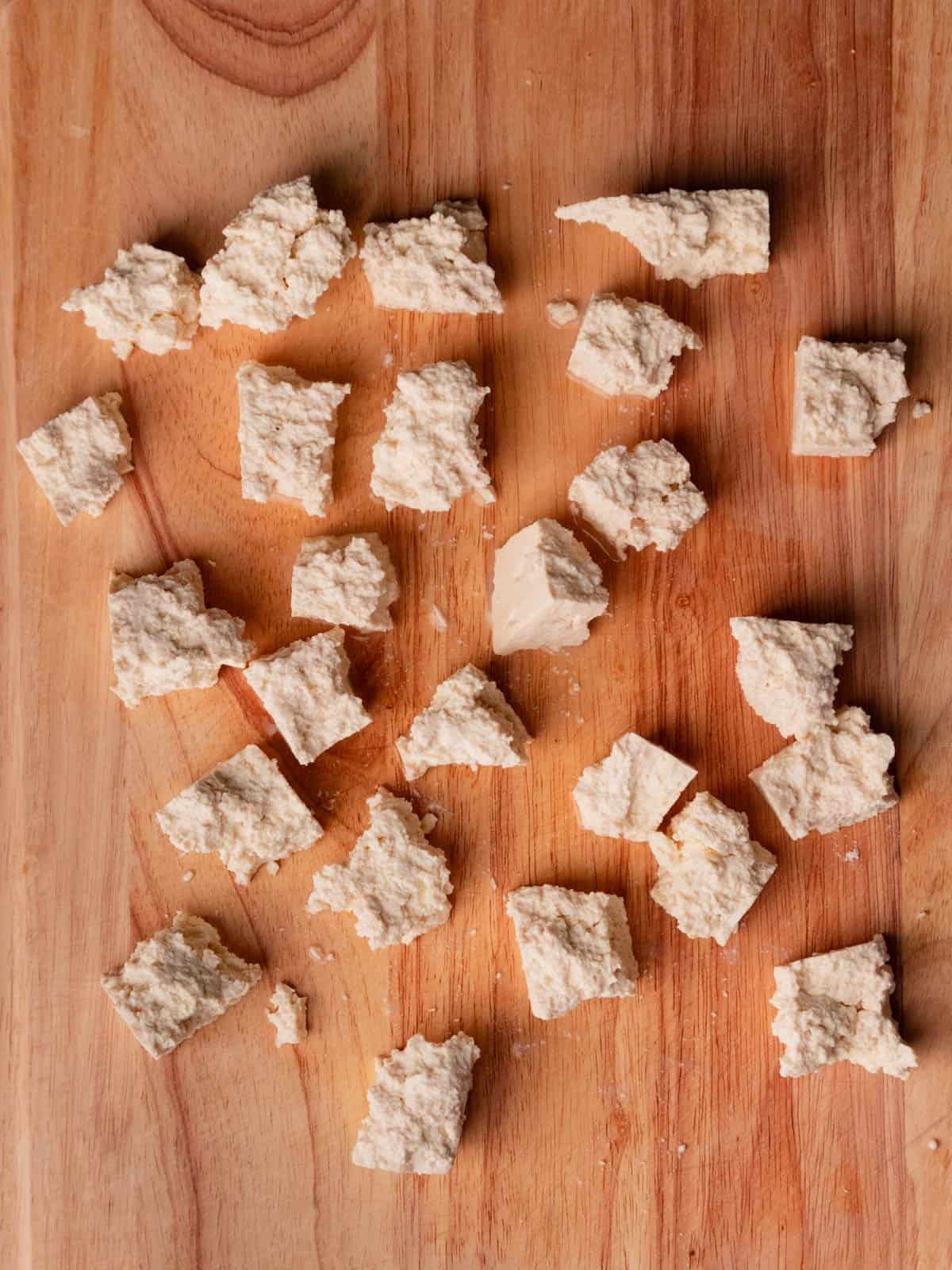 Cubes of ripped tofu on a wooden cutting board.