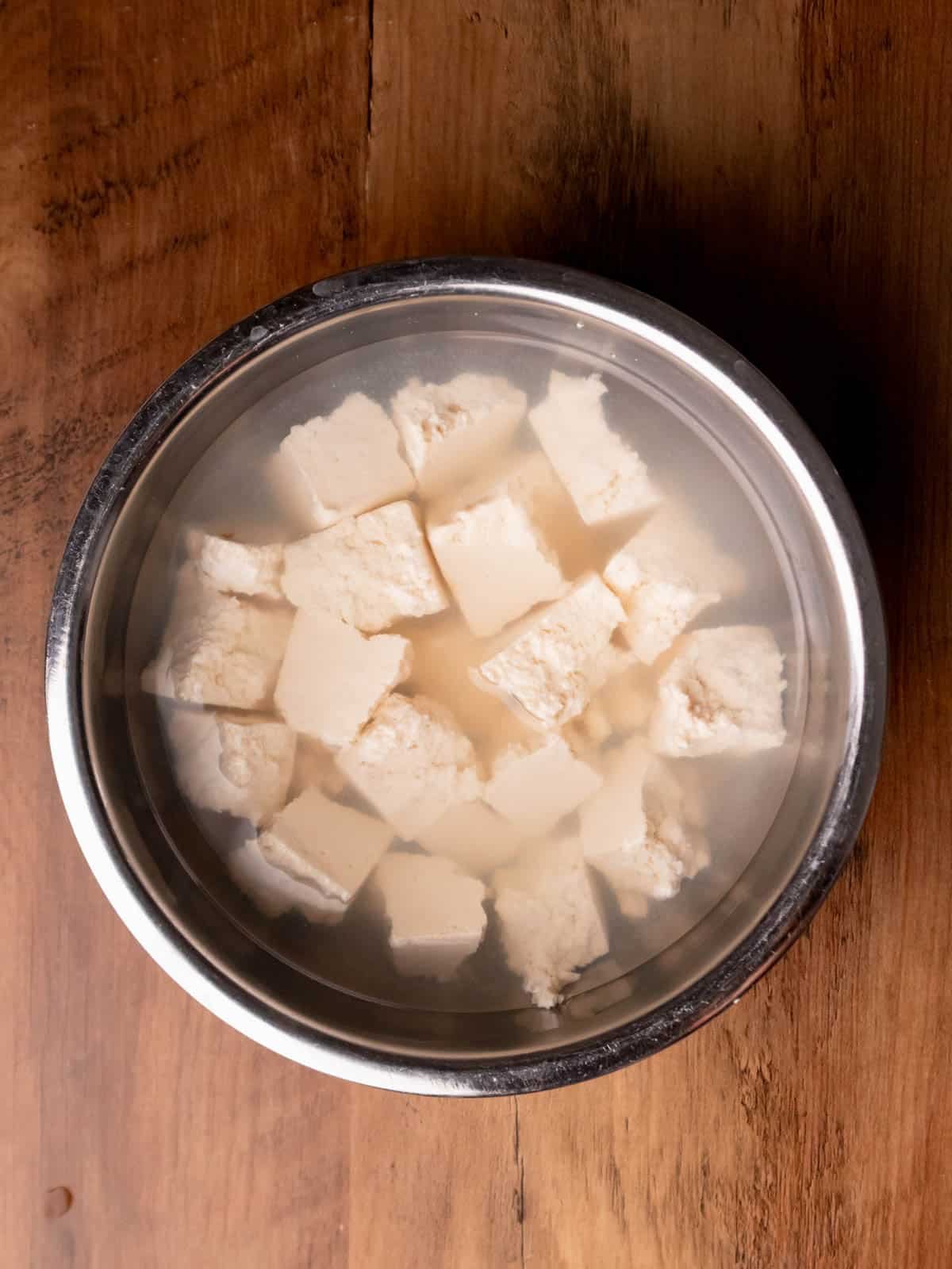 Ripped firm tofu soaking in salt water in a silver bowl.
