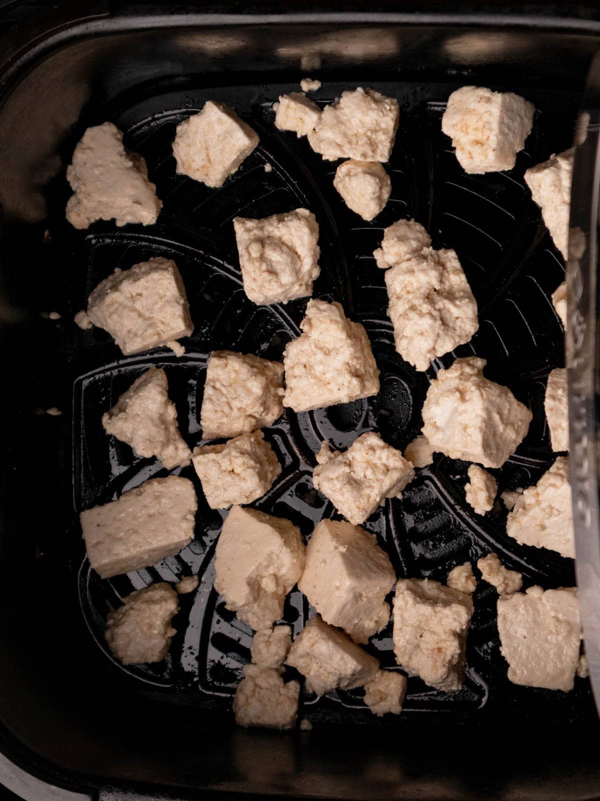 Raw seasoned ripped tofu in an air fryer tray.