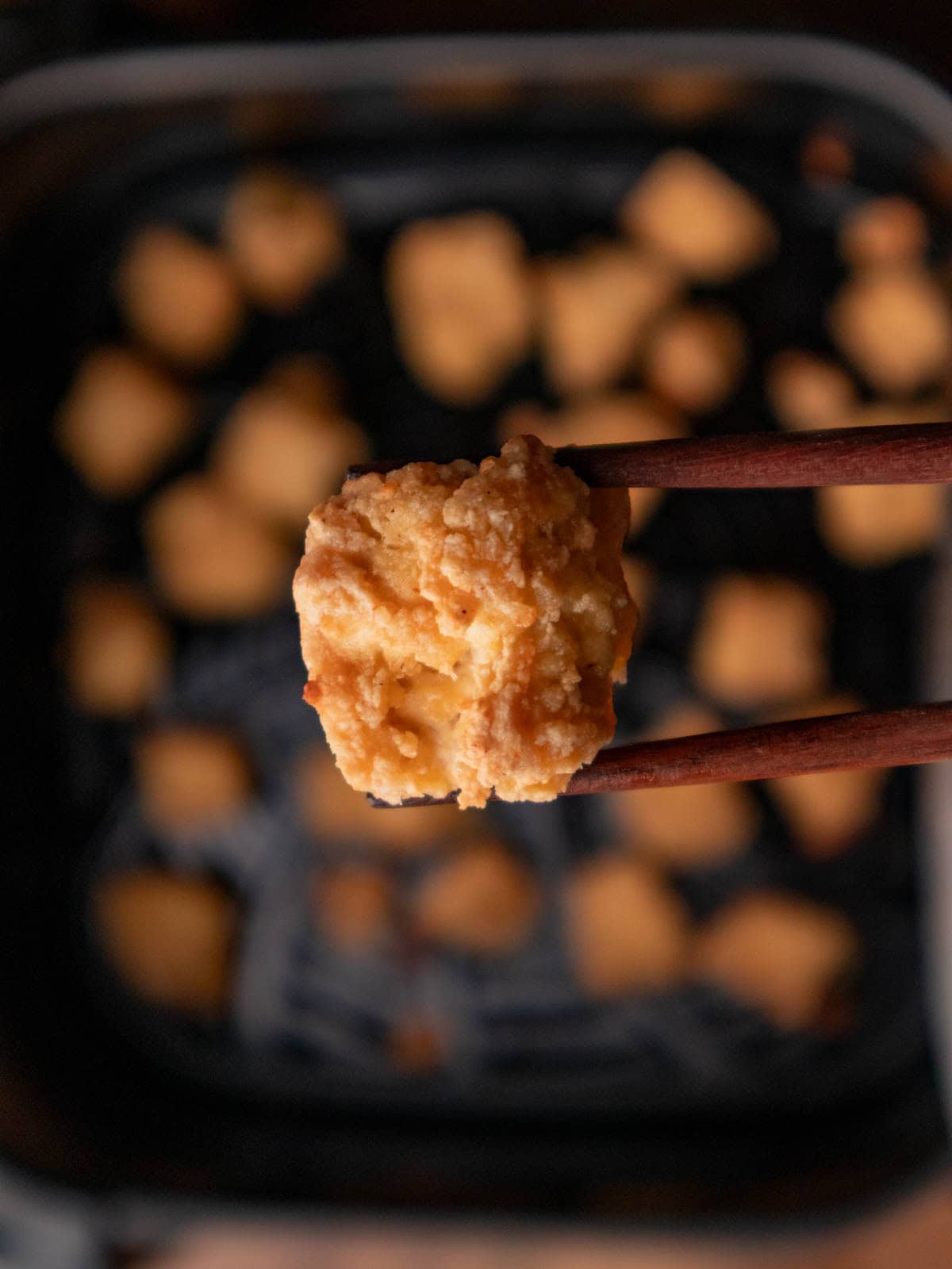 Crispy golden tofu help by wooden chopsticks over air fryer tray.