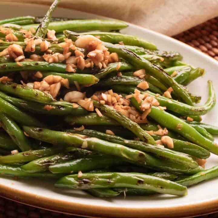 White brown rimmed oval plate with green bean stir-fry topped with browned garlic.