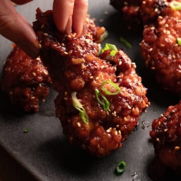 Korean fried chicken topped with sesame seeds & green onions on a black plate.