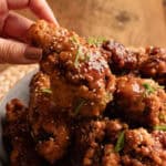 Fingers picking up soy garlic Korean fried Chicken from a plate.