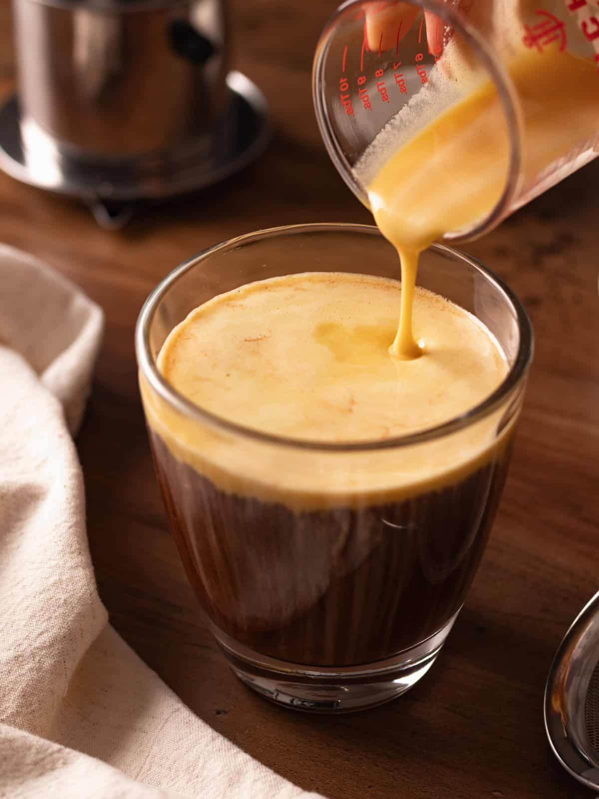 Drizzling egg topping into a glass cup of Vietnamese coffee.