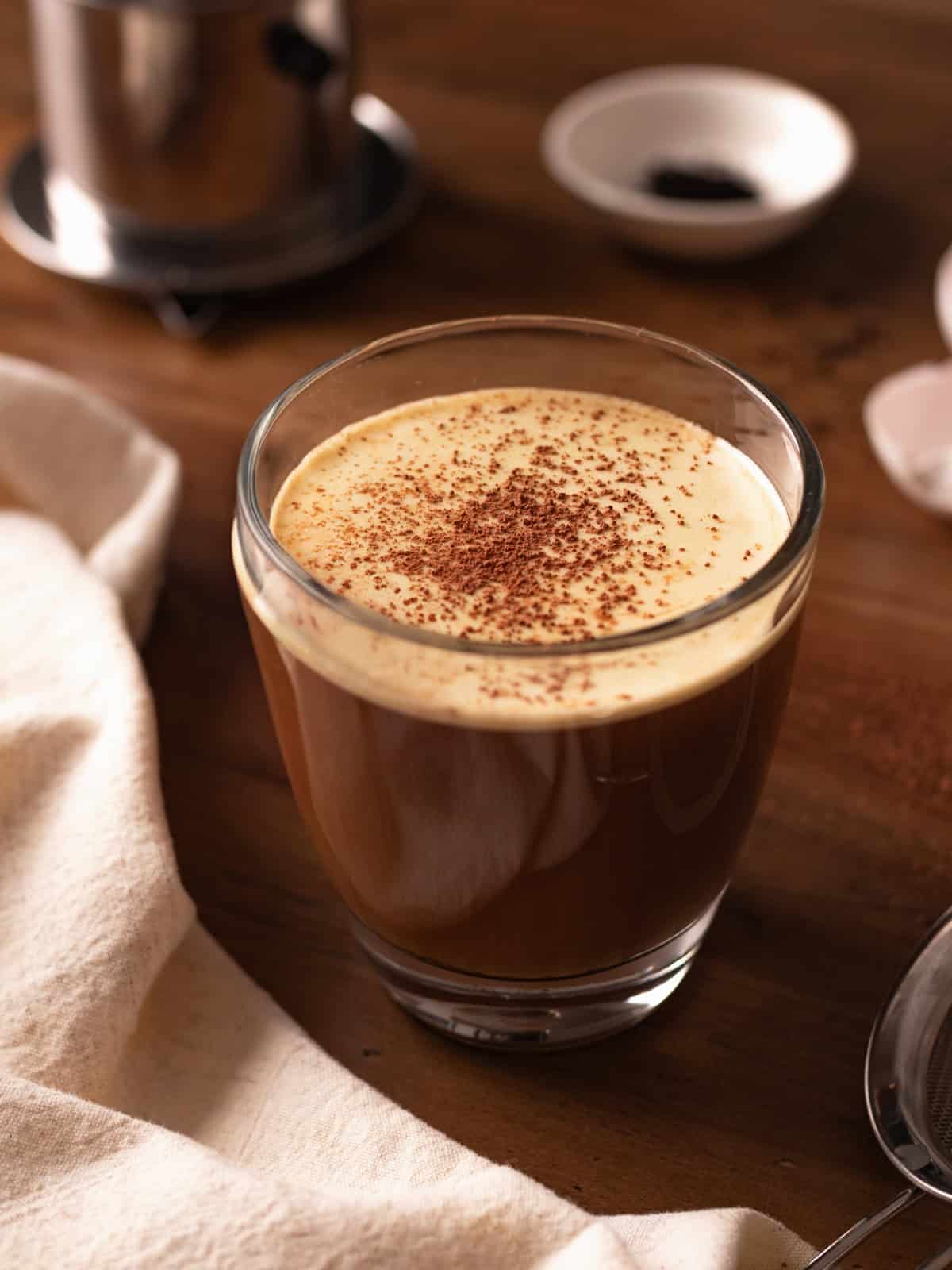 Glass cup of Vietnamese egg coffee topped with cocoa powder.