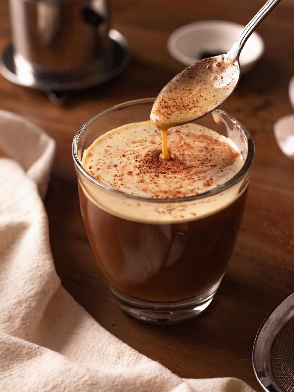 Spoon dripping egg topping in glass cup of Vietnamese egg coffee.