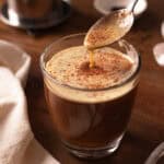 Spoon dripping egg topping in glass cup of Vietnamese egg coffee.