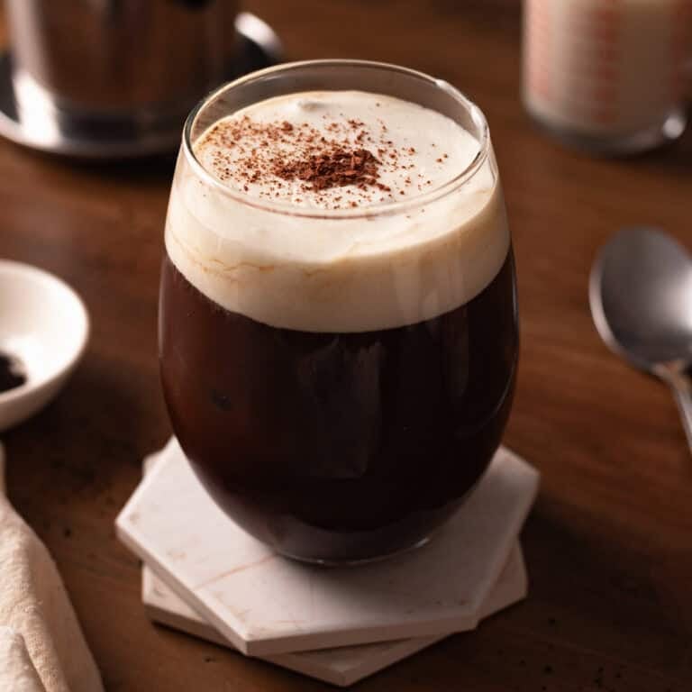 Glass of salted coffee topped with cocoa powder on white coasters.