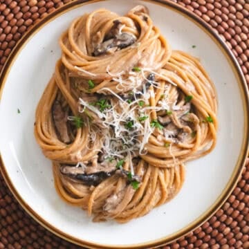 Miso mushroom pasta with shredded parmesan on a white brown rimmed plate.