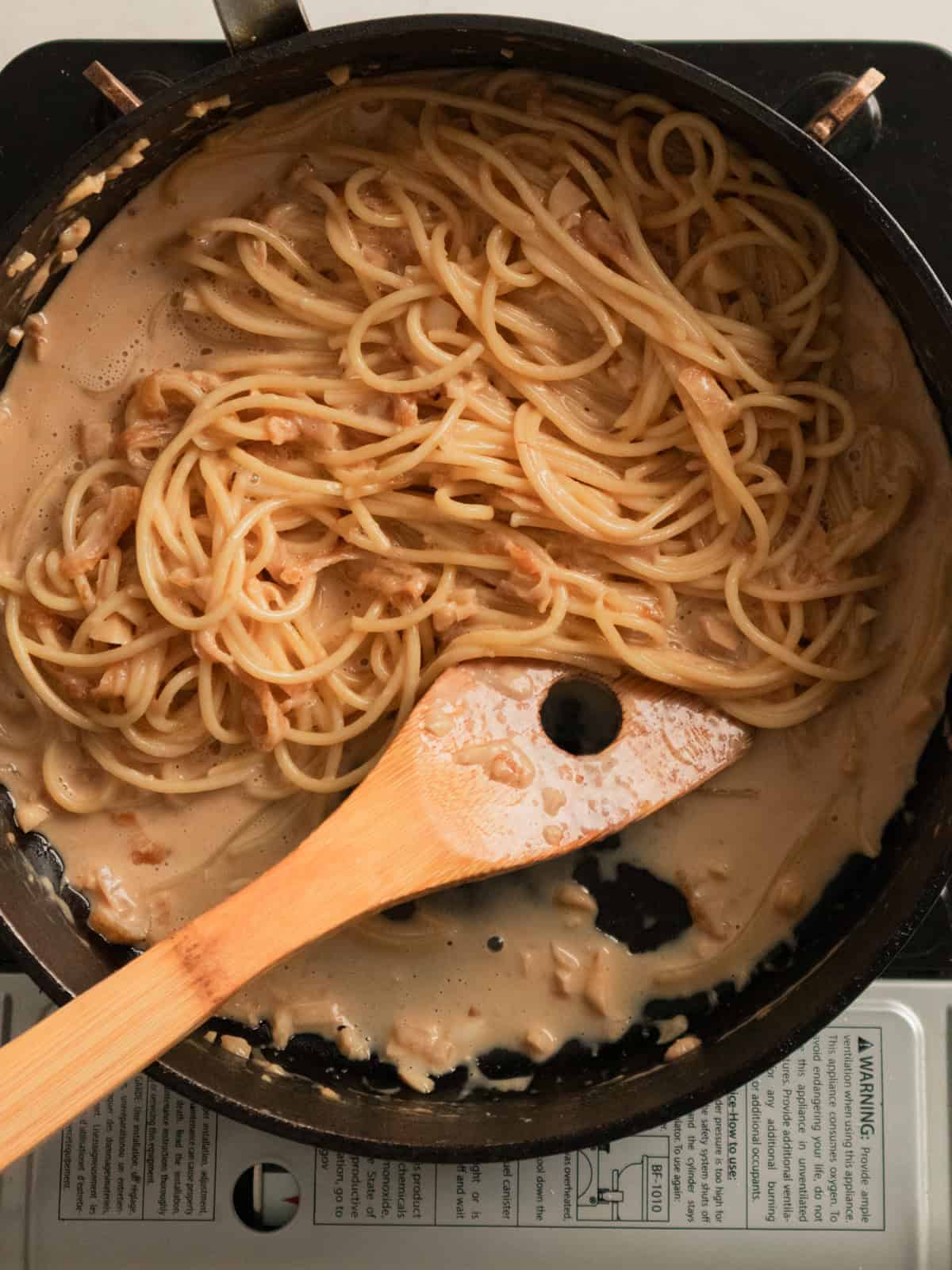 Spaghetti noodles mixed in miso pasta sauce in a black pan.
