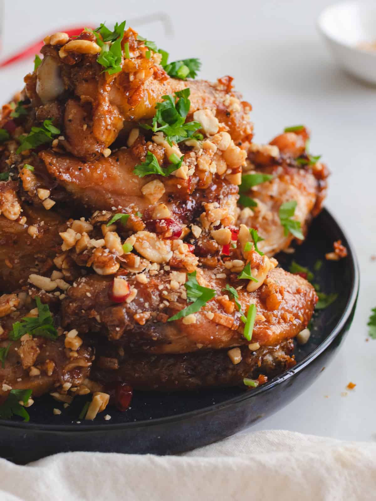 Tamarind chicken wings with crushed peanuts, cilantro, and chilies on a blue plate.