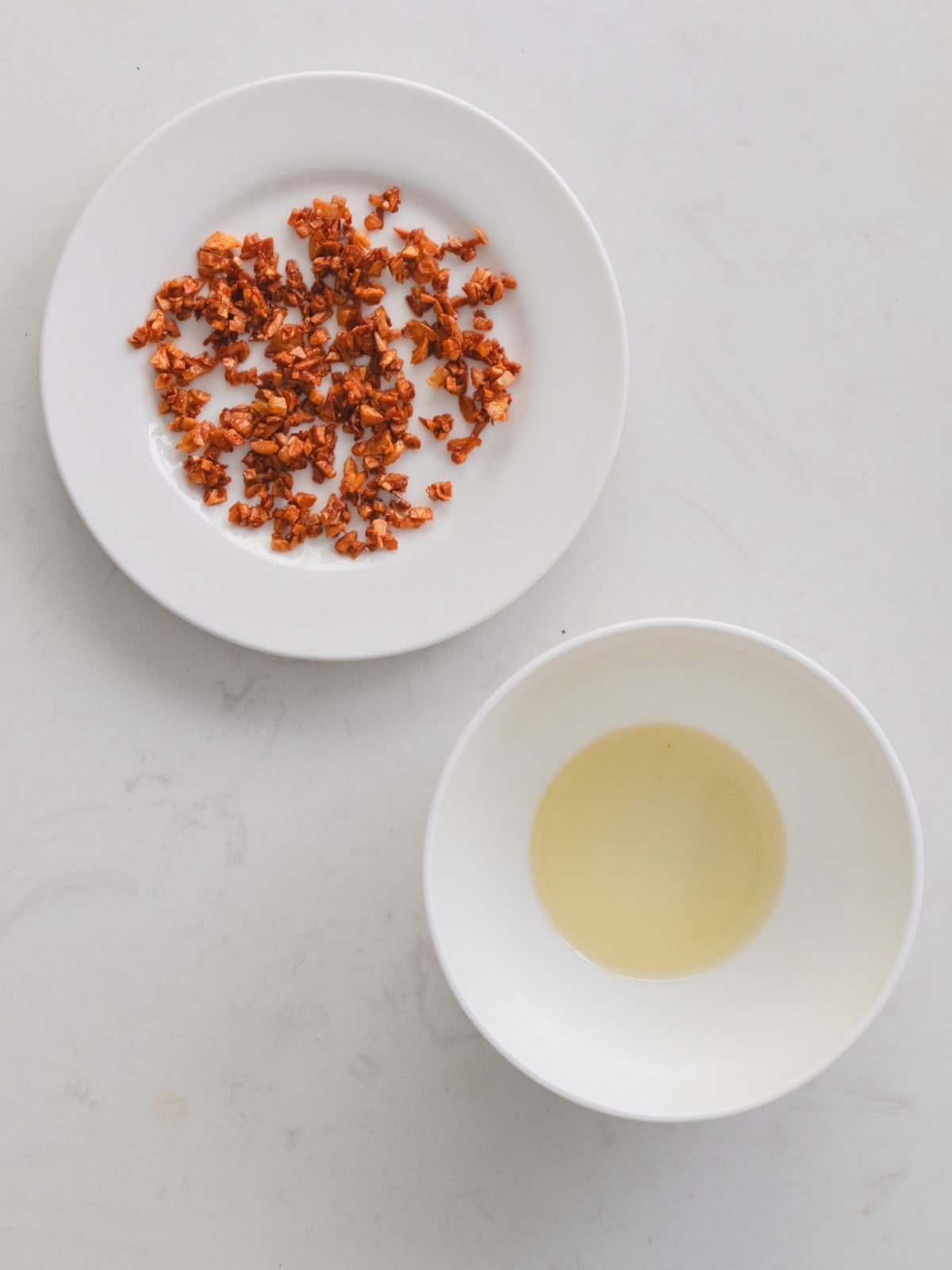 Golden garlic crisps on a white plate with garlic oil in a small bowl.