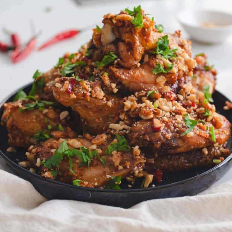 Tamarind chicken wings with crushed peanuts, cilantro, and chilies on a blue plate.