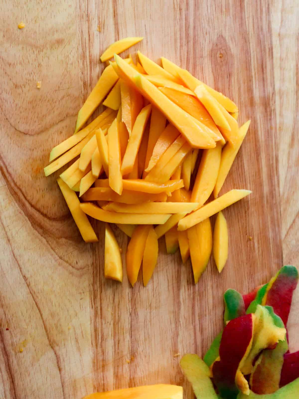 Green mangoes sliced into matchsticks on a wooden cutting board.
