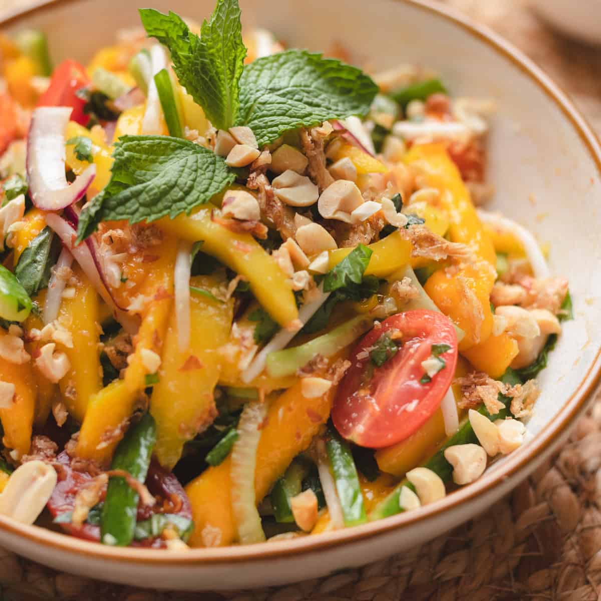 Green mango salad in a brown rimmed white bowl garnished with herbs & crushed peanuts.