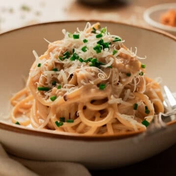 Miso pasta in a white and brown rimmed bowl with chives and parmesan.