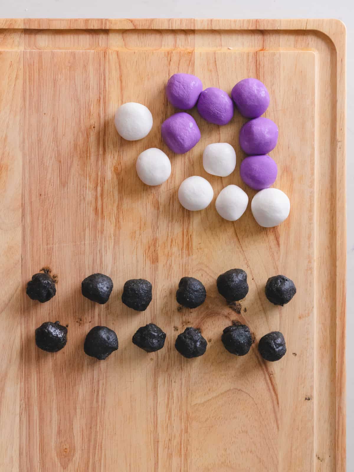 Wooden cutting board of glutinous rice balls and balls of black sesame paste next to each other.