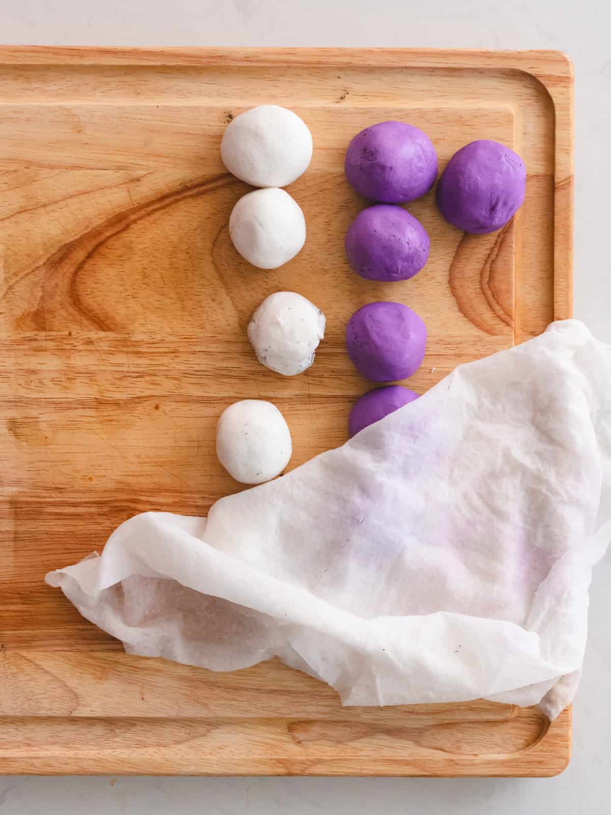 Wooden cutting board with glutinous rice balls filled with black sesame paste.