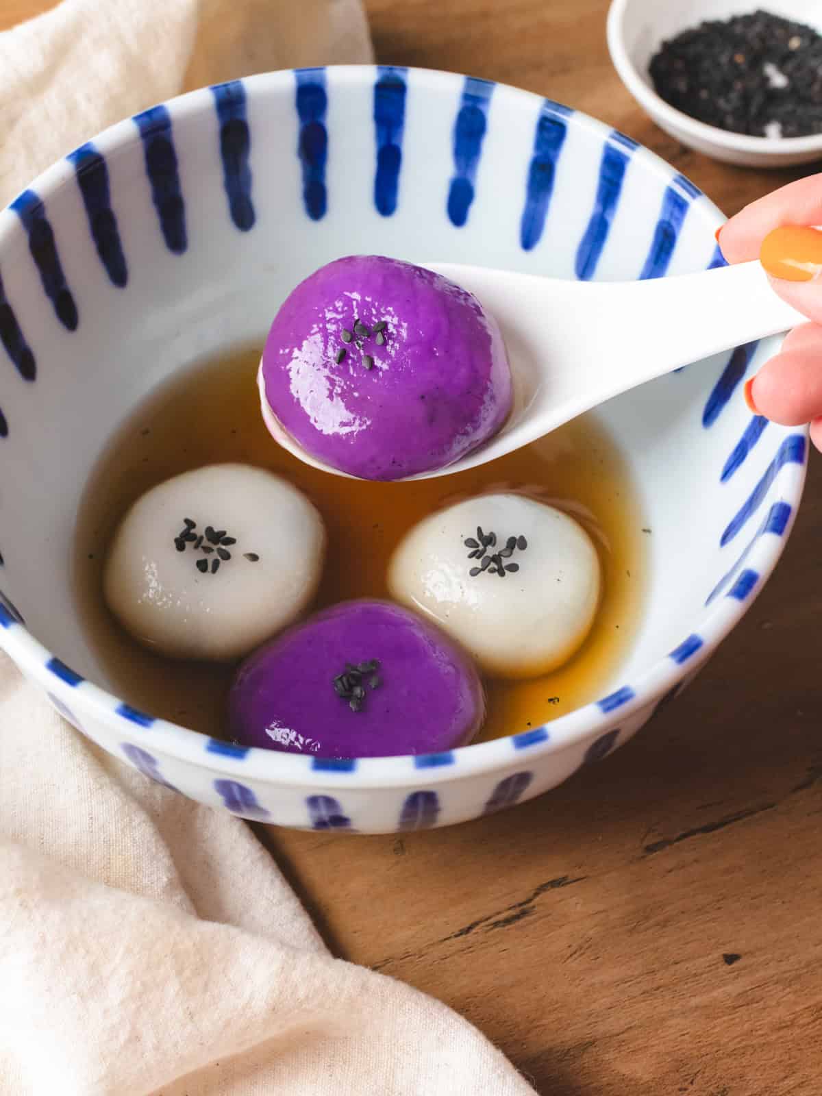 Spoon of glutinous rice balls in ginger syrup in a blue striped bowl.