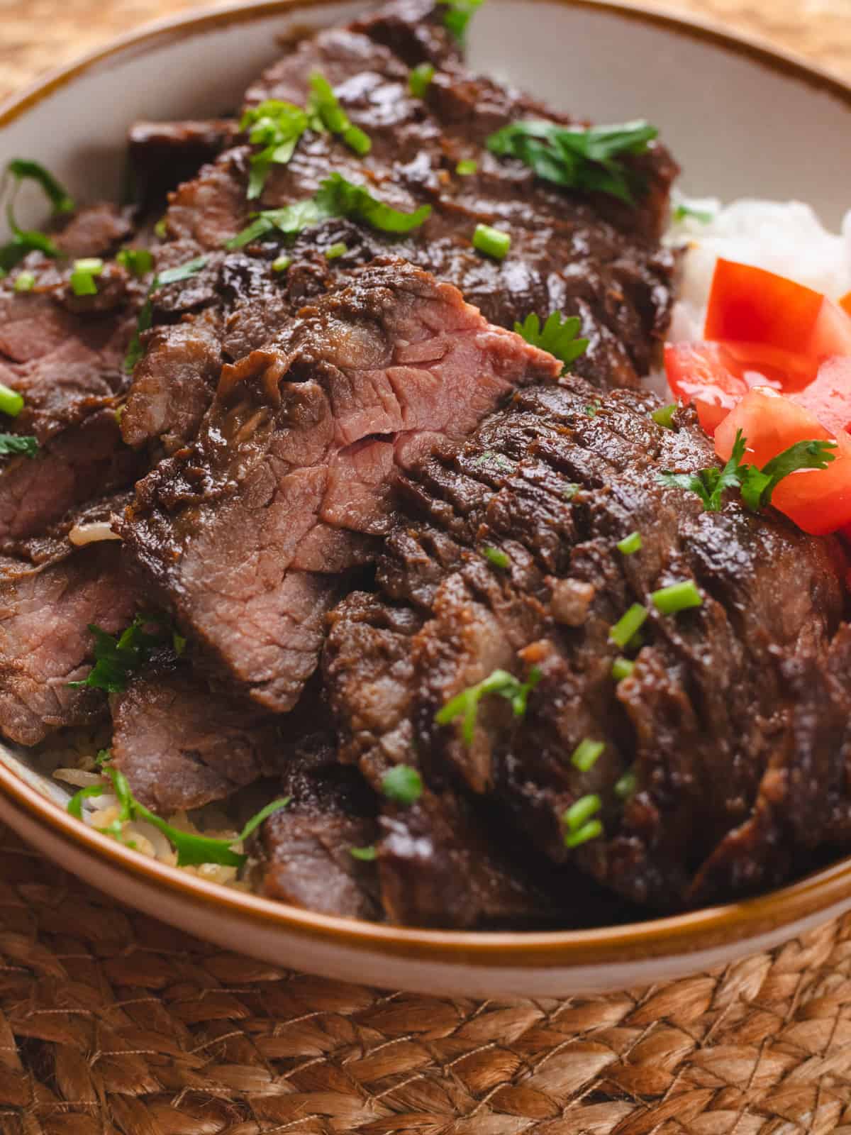 Asian marinated skirt steak on white rice and side of tomatoes.
