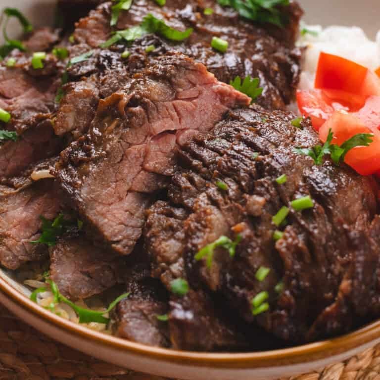 Asian marinated skirt steak on white rice and side of tomatoes.