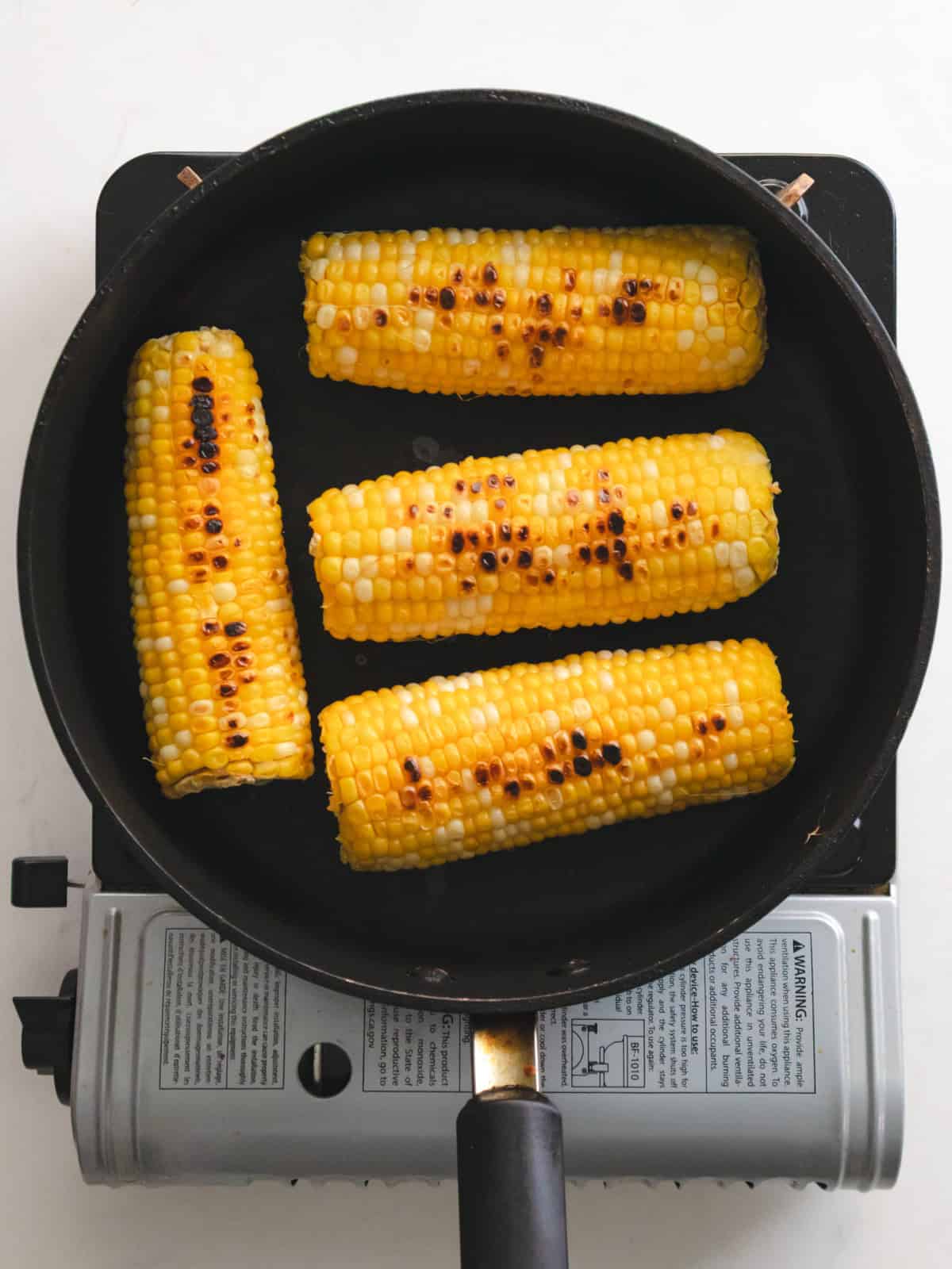 Corn on the cob cooking on a skillet stovetop.