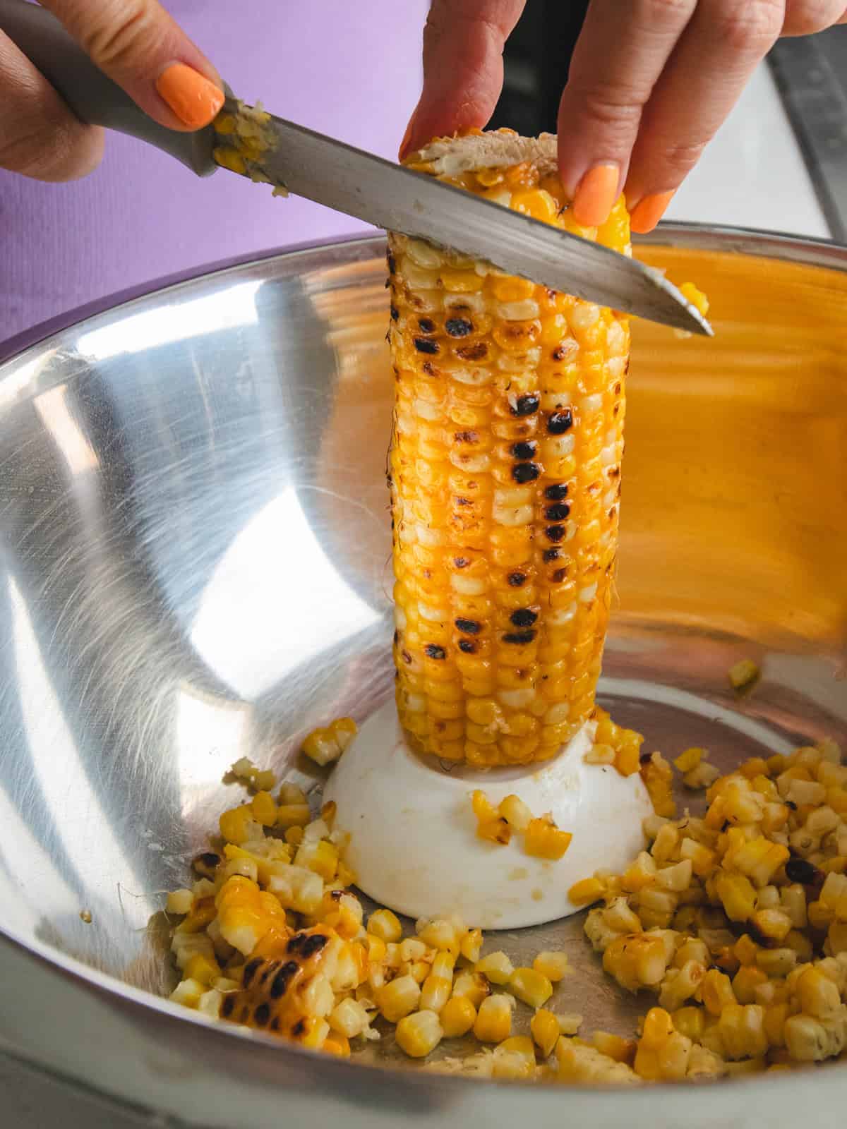 Corn on the cob being sliced off the cob in a silver bowl.