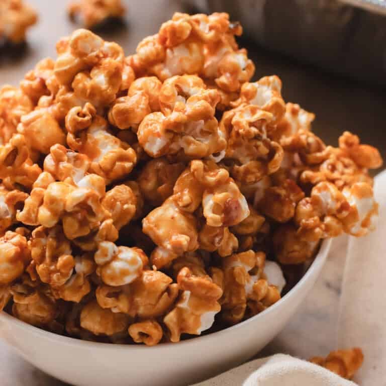 Homemade miso caramel popcorn in a white bowl on a wood table.