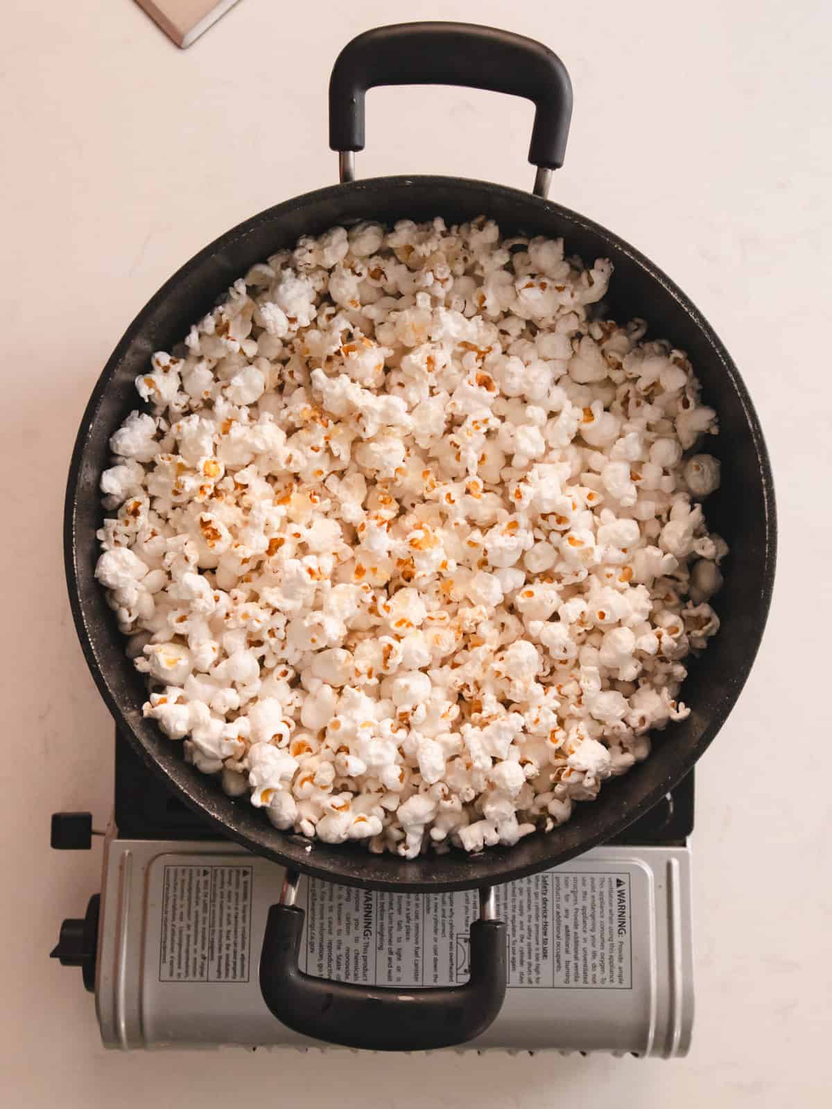 Black pot of popped popcorn on a white kitchen counter.