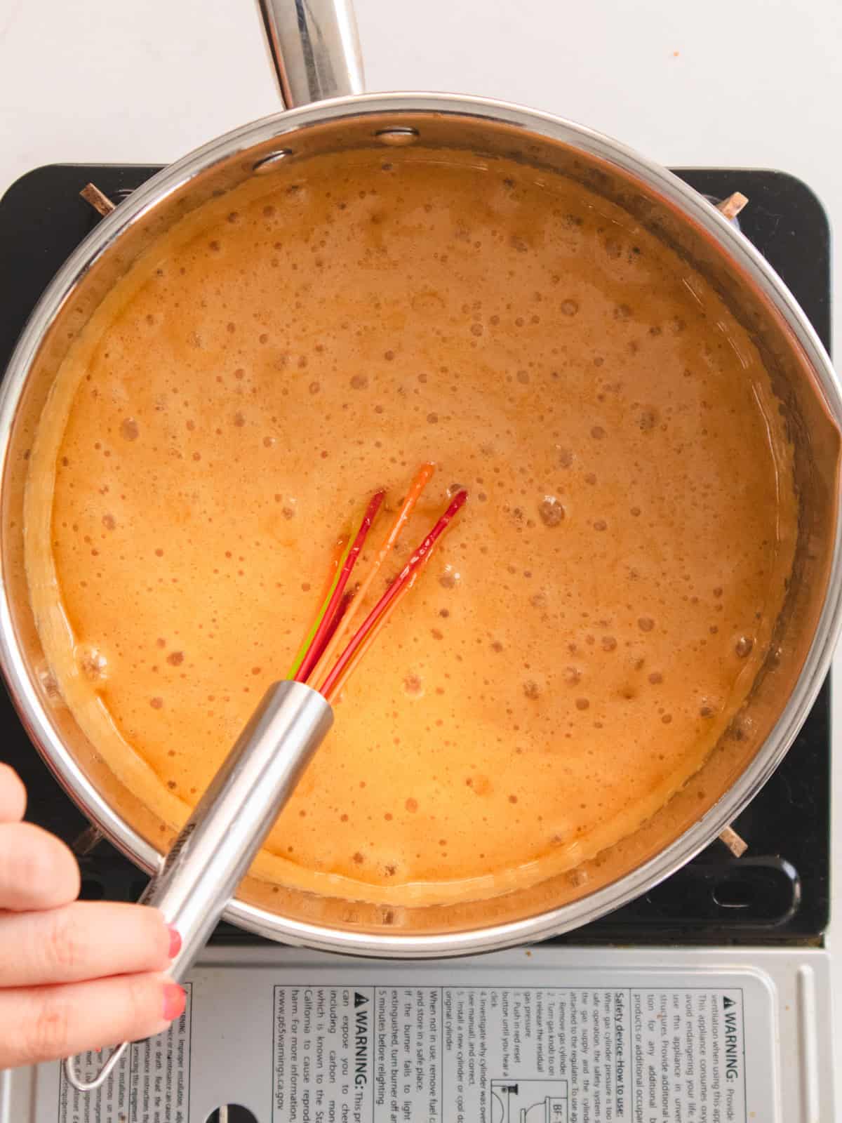 Frothy miso caramel whisked in a stainless steel pot.